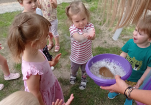 Anulka trzyma magiczną bańkę mydlaną z zawartym w niej dymkiem. Wokół są obserwujące dzieci.